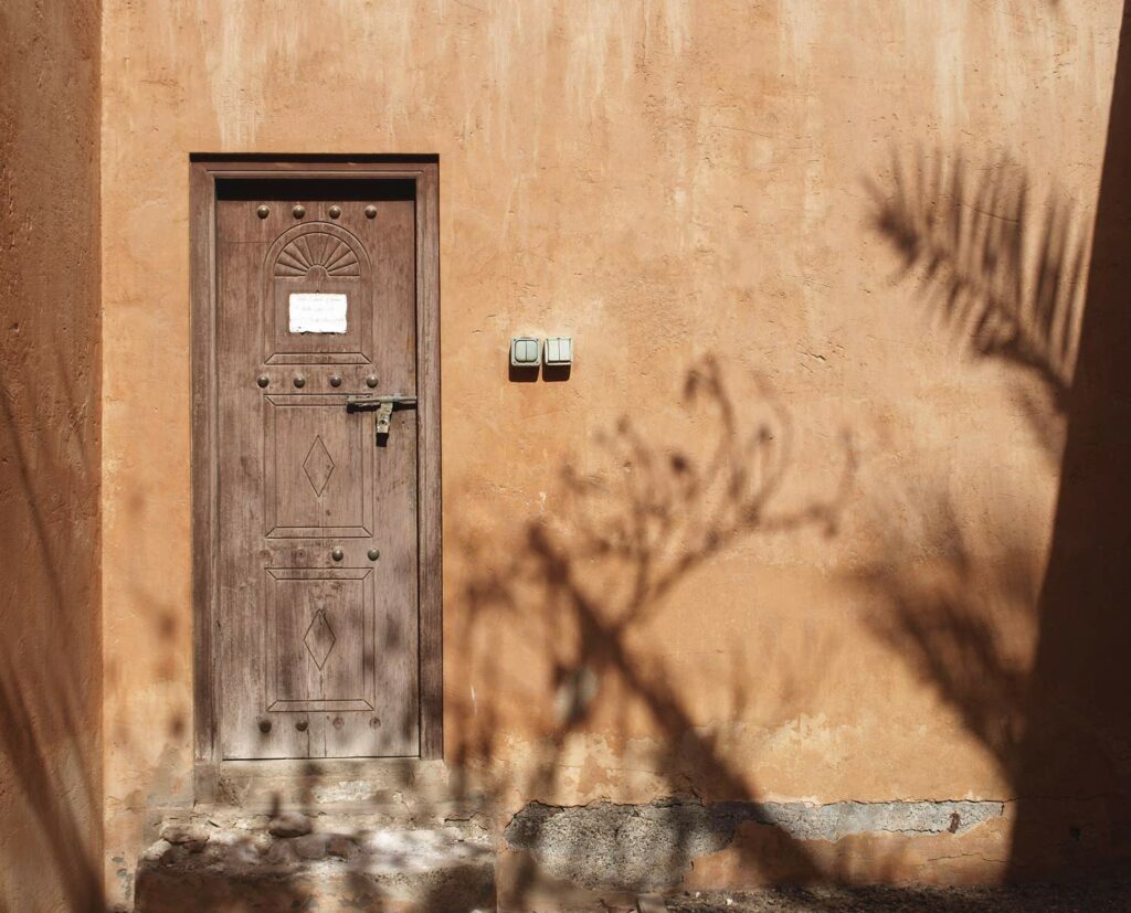 colorful photograph of an orange arab building with brown door and shadows